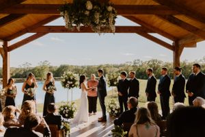 A sunset wedding ceremony takes place under a wooden pavilion with guests watching.