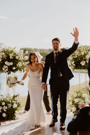 Newlyweds celebrate with raised arms after their ceremony under a floral arch.