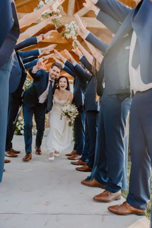 Groomsmen in blue suits form an arch tunnel for the newlyweds to walk through.