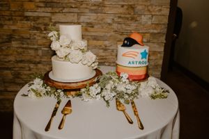 White wedding cake and desserts displayed on round table with golden utensils and floral decorations.