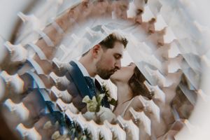 Artistic wedding photo taken through flower petals showing couple sharing a romantic moment.
