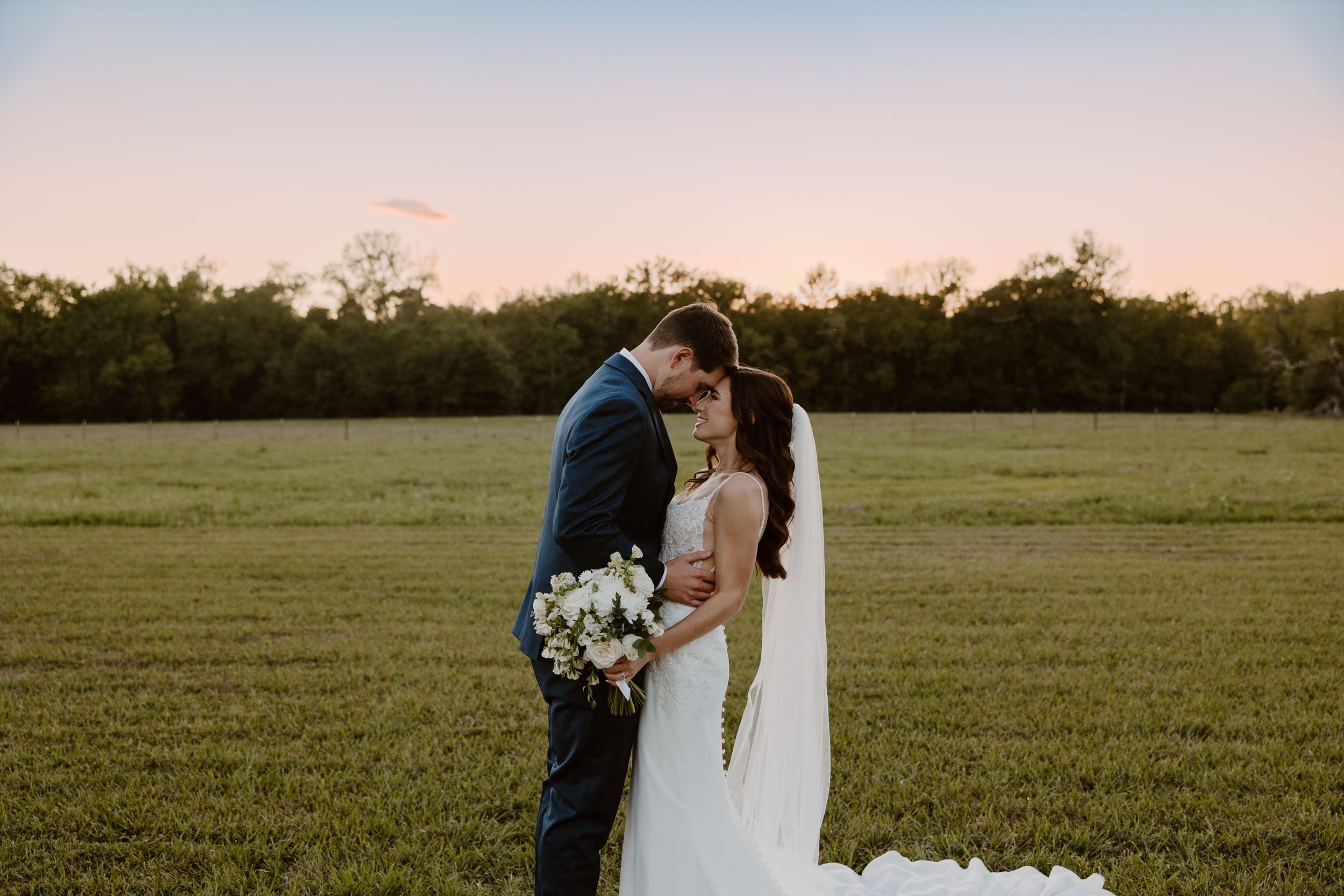 Wedding couple embracing in open field during golden hour with dramatic lighting.