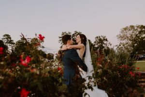 Sunset garden wedding photo with red flowers in foreground and couple sharing an intimate moment.
