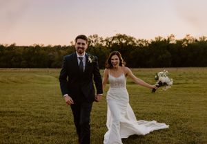 Joyful newlyweds running hand in hand across grassy field during golden hour.