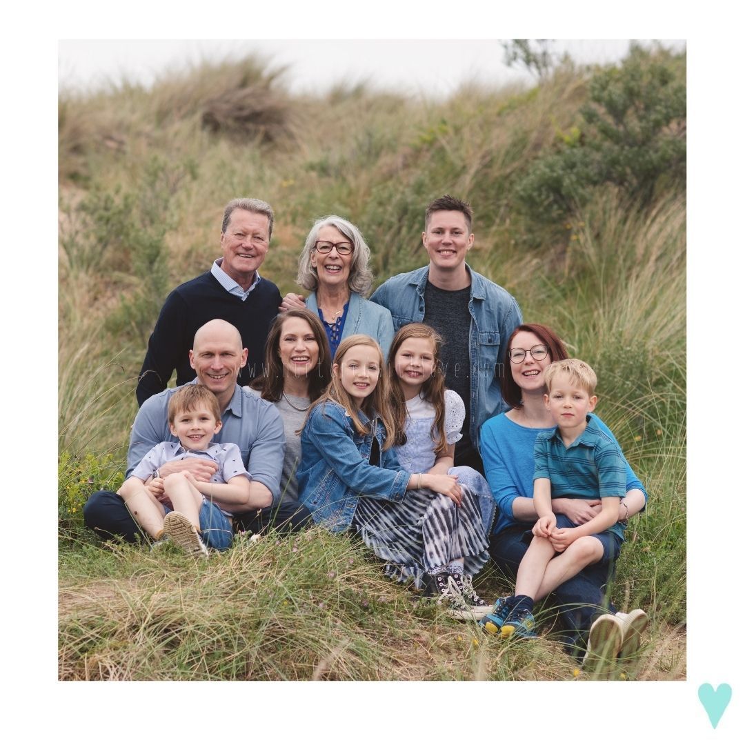 Multi-generational family portrait taken outdoors on a grassy hillside.