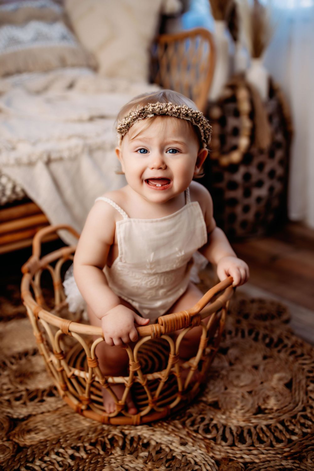 Baby sitting in wicker basket wearing cream dress and floral crown.