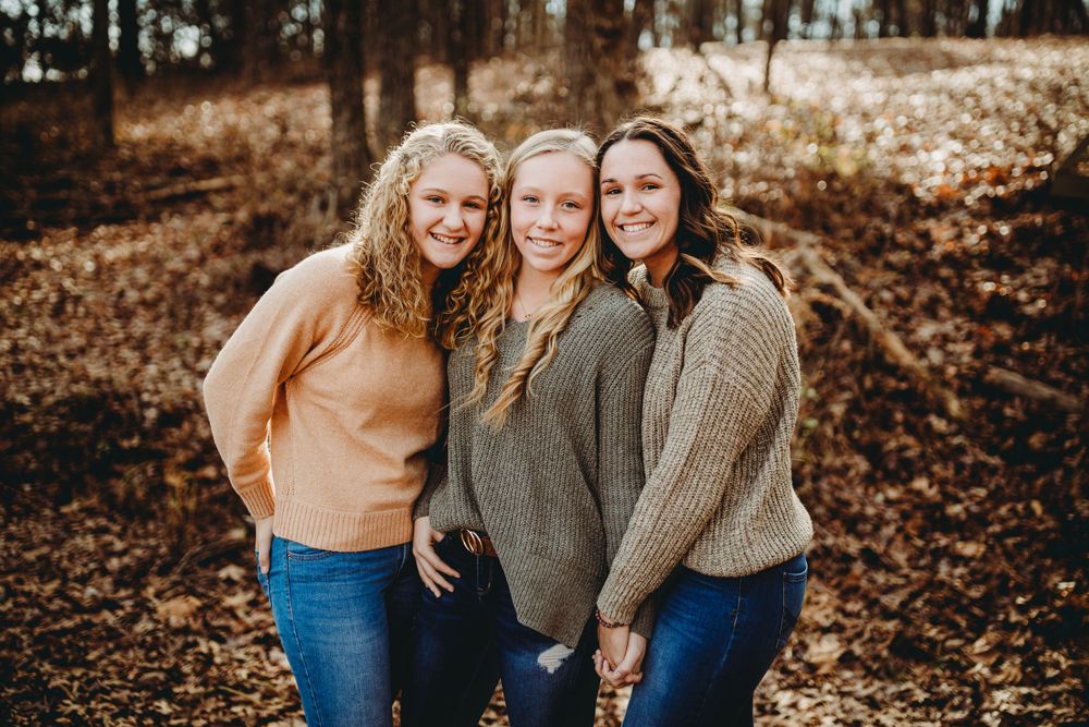 Three women in sweaters posing together in autumn woods.