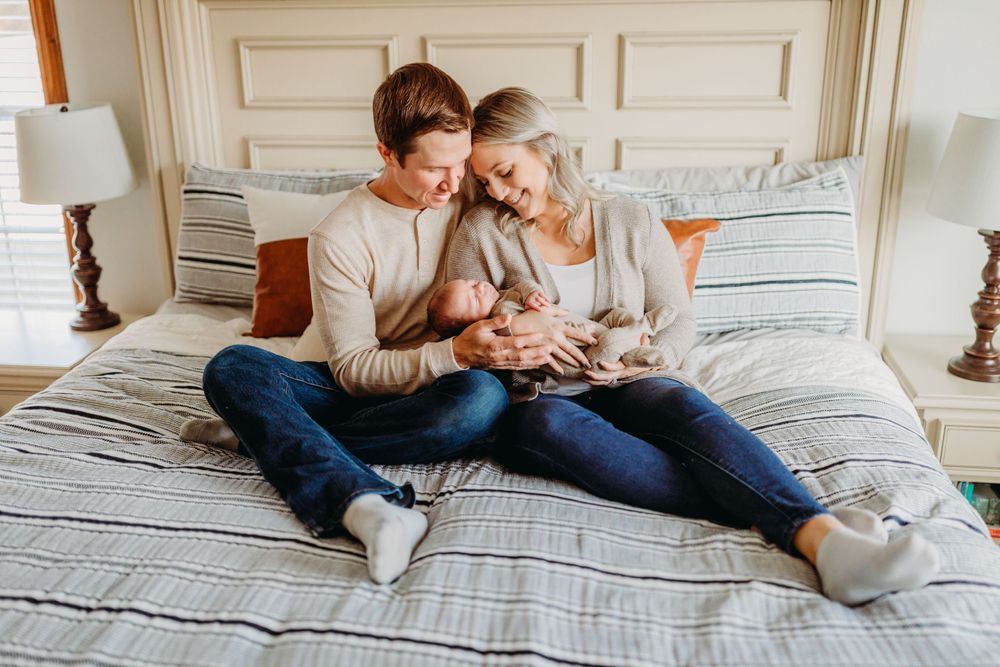A tender moment shared while sitting together on a bed with a small baby amongst white linens.