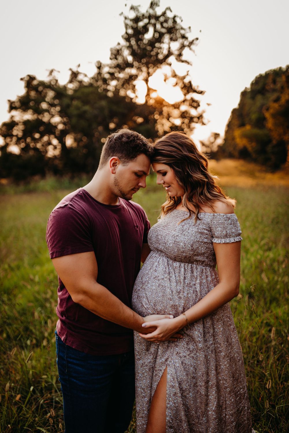 Romantic maternity portrait of couple in field at sunset.