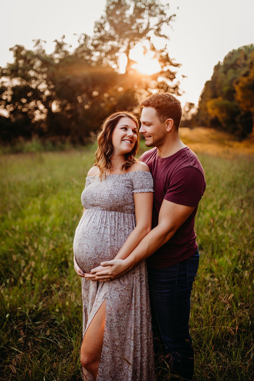 Intimate maternity photo of couple embracing in golden sunset field.