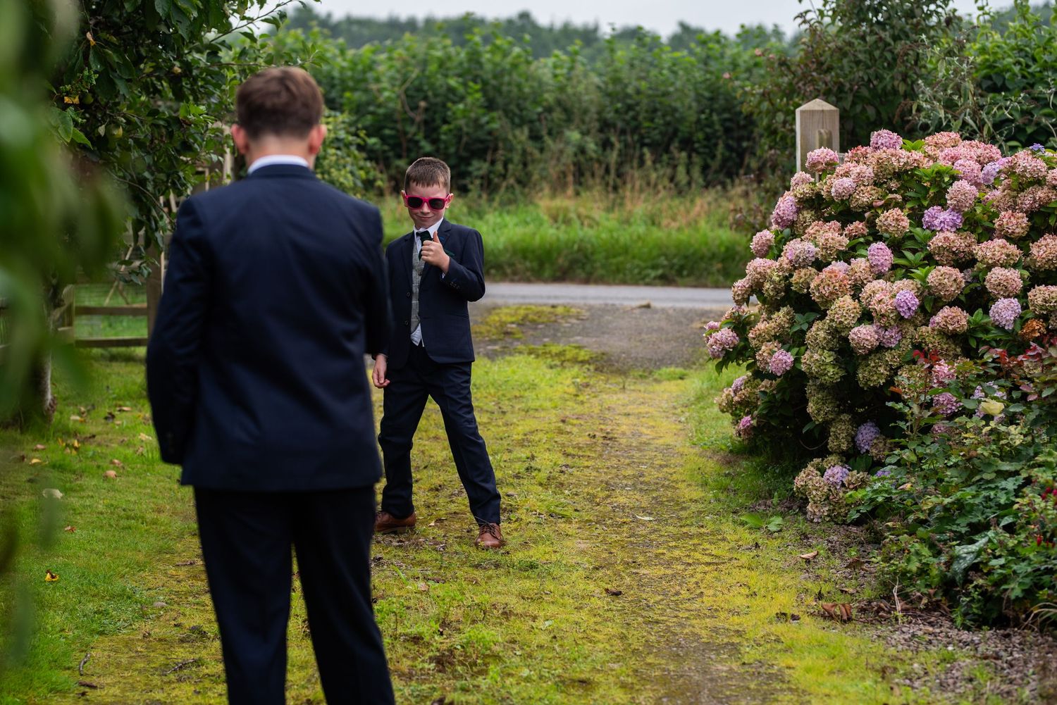Two people in formal attire having conversation near blooming hydrangea bush in garden.