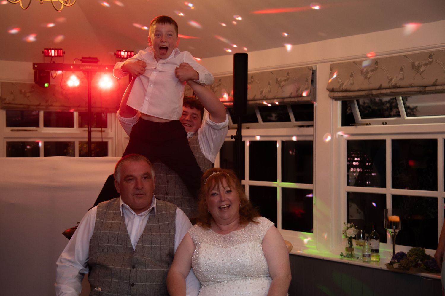 Wedding guests dancing and celebrating at an indoor reception with red lighting effects.