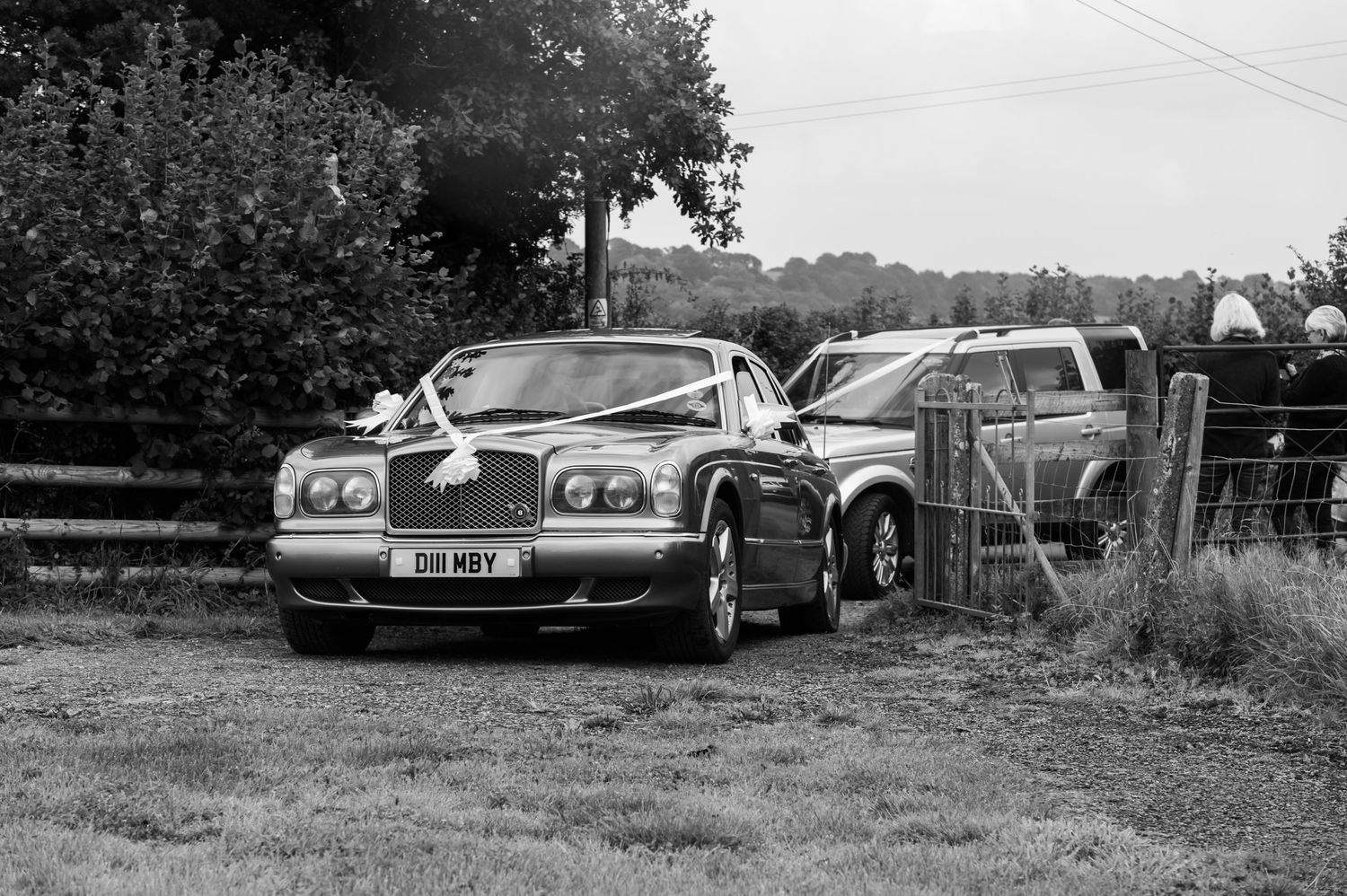 Classic cars parked in a grassy field at an outdoor wedding venue.