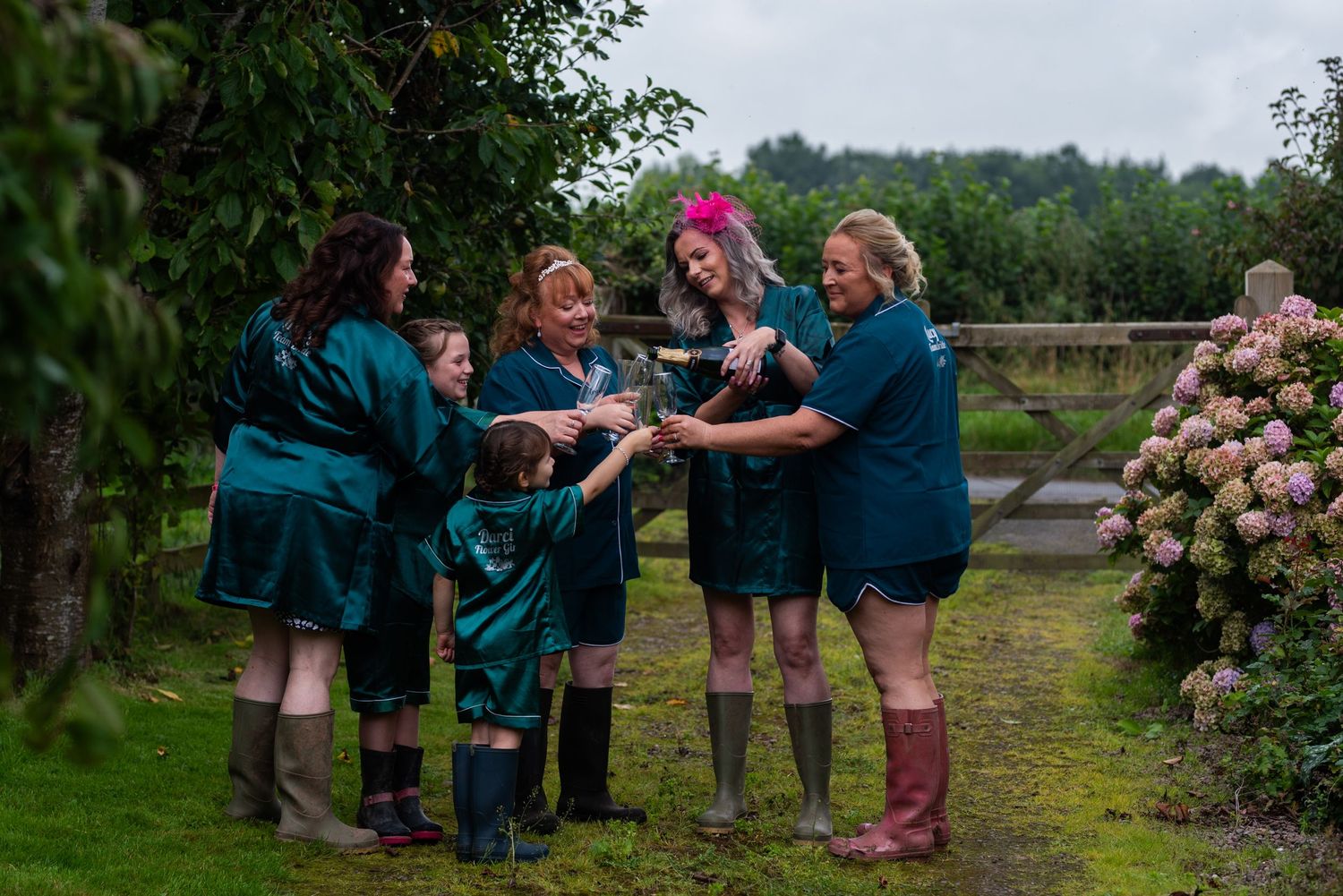 Wedding guests celebrating outdoors in teal colored attire surrounded by blooming hydrangea bushes.