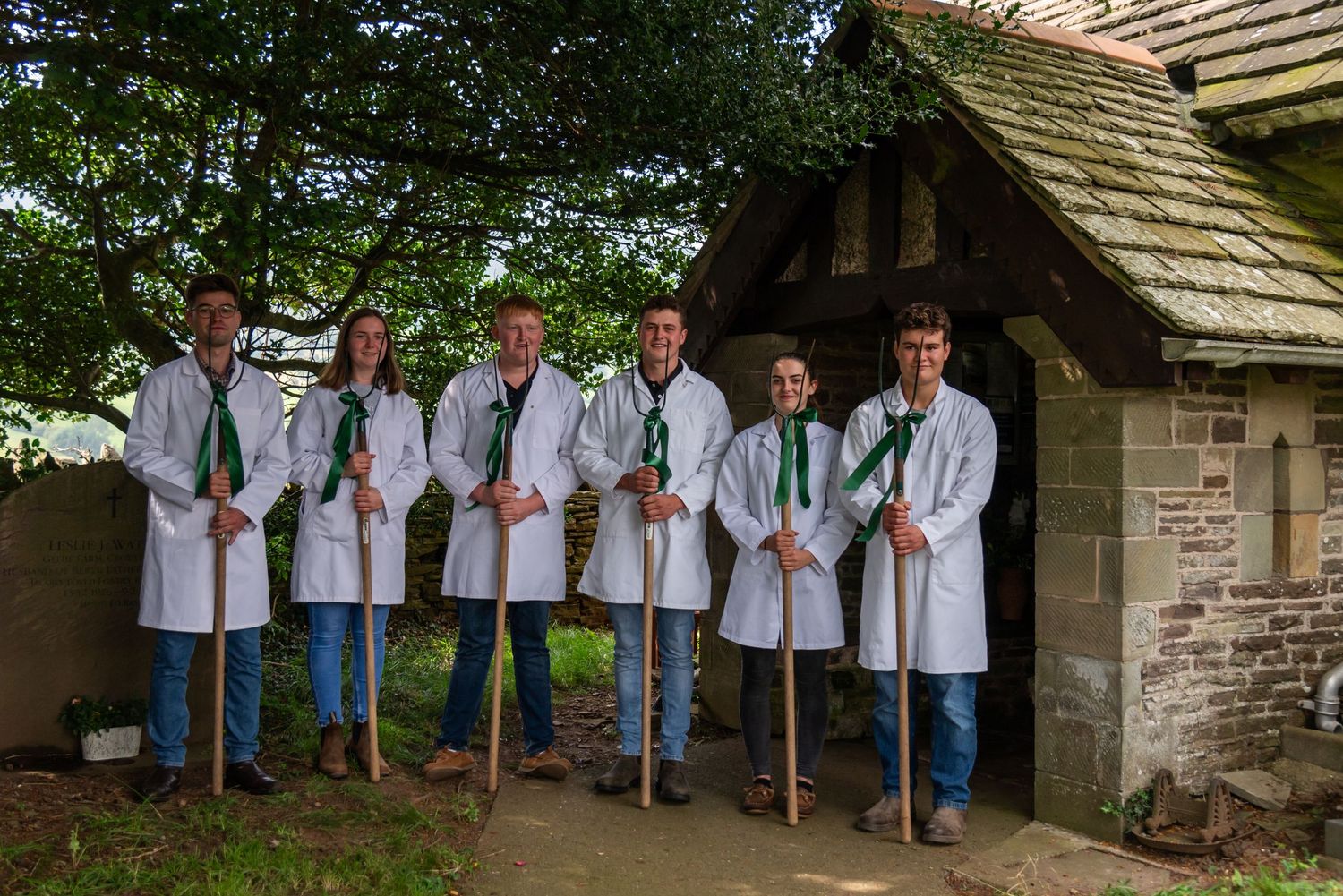 Groomsmen lined up against a rustic stone wall wearing white shirts and jeans.