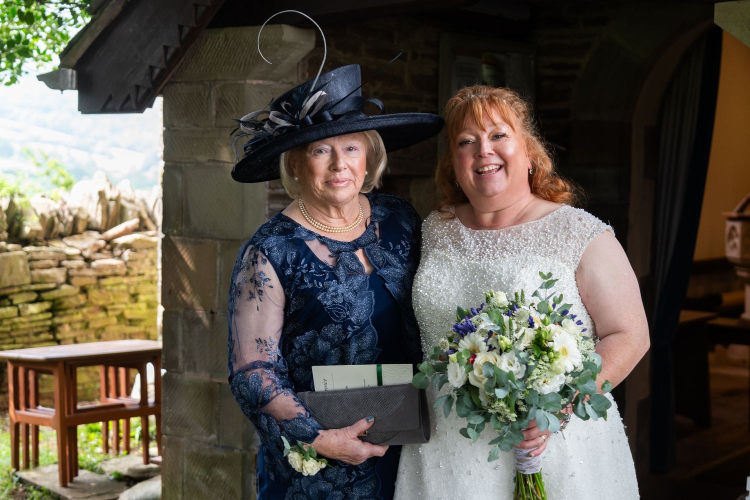 Wedding party gathered outside a stone building in formal teal and white attire.