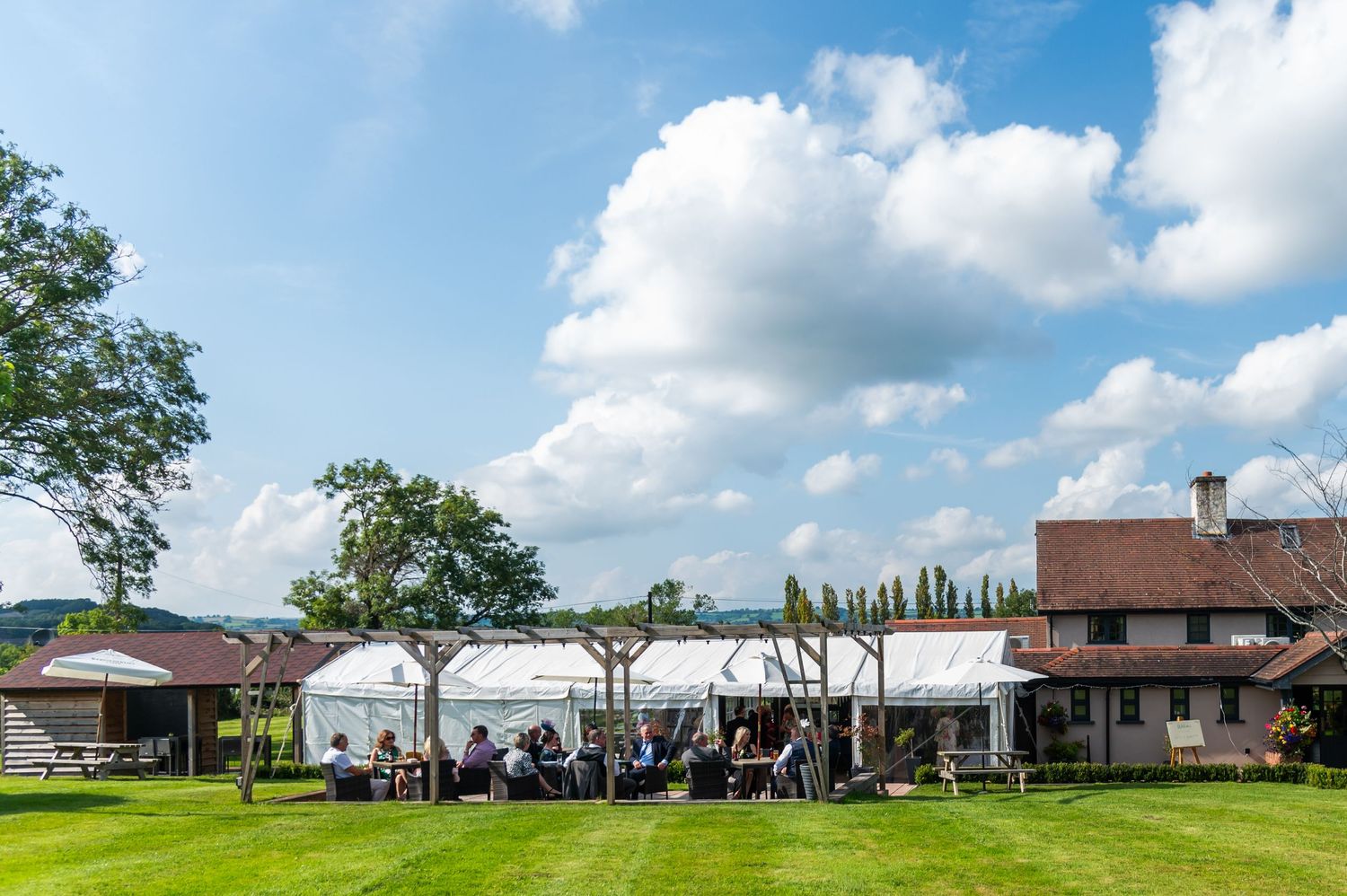 White party tent set up on green lawn with venue building in background under blue summer sky.