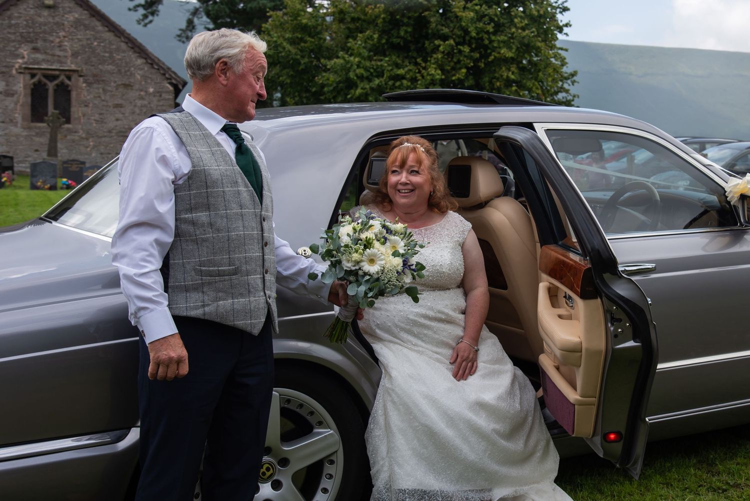 Wedding party arriving in elegant black cars outside a stone church building.