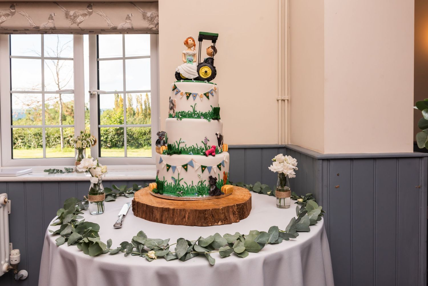 Wedding reception table decorated with rustic wood centerpieces and green floral garlands.