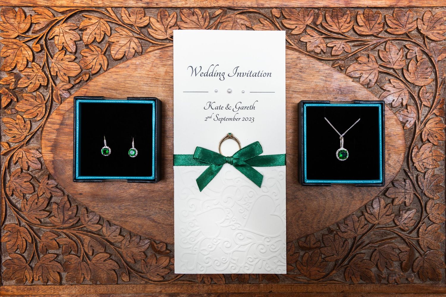 Wedding invitations and jewelry displayed on carved wooden background.
