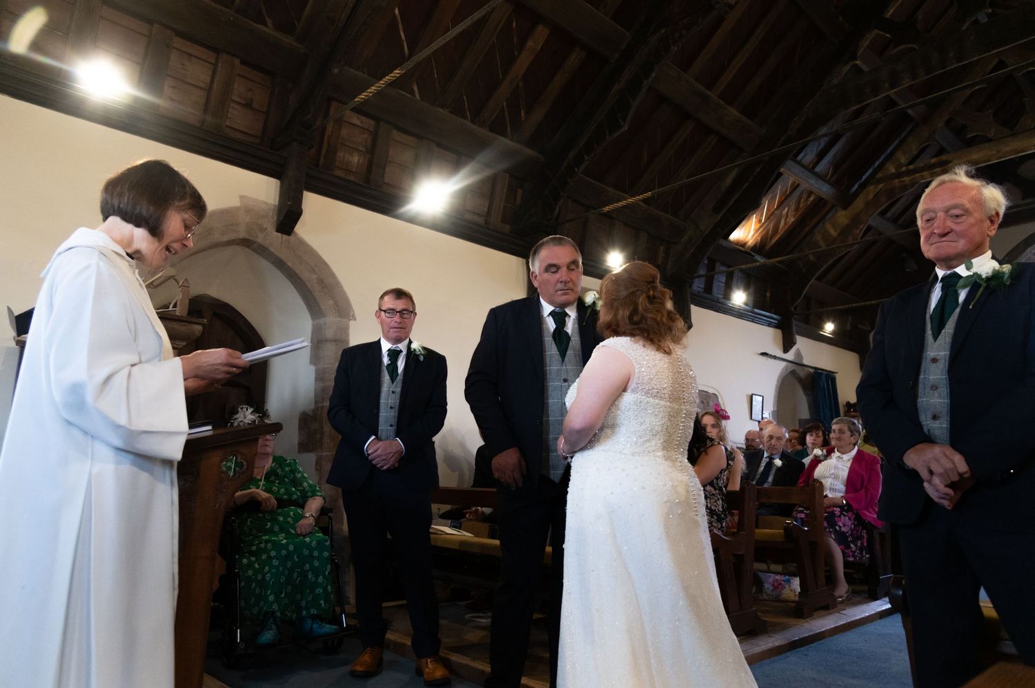 Wedding ceremony taking place inside historic church with exposed wooden beams and arched ceiling.