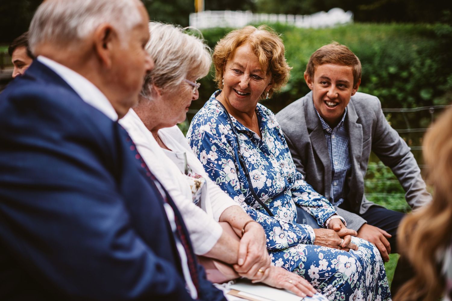 Wedding guests share a light moment while seated outdoors during the ceremony.