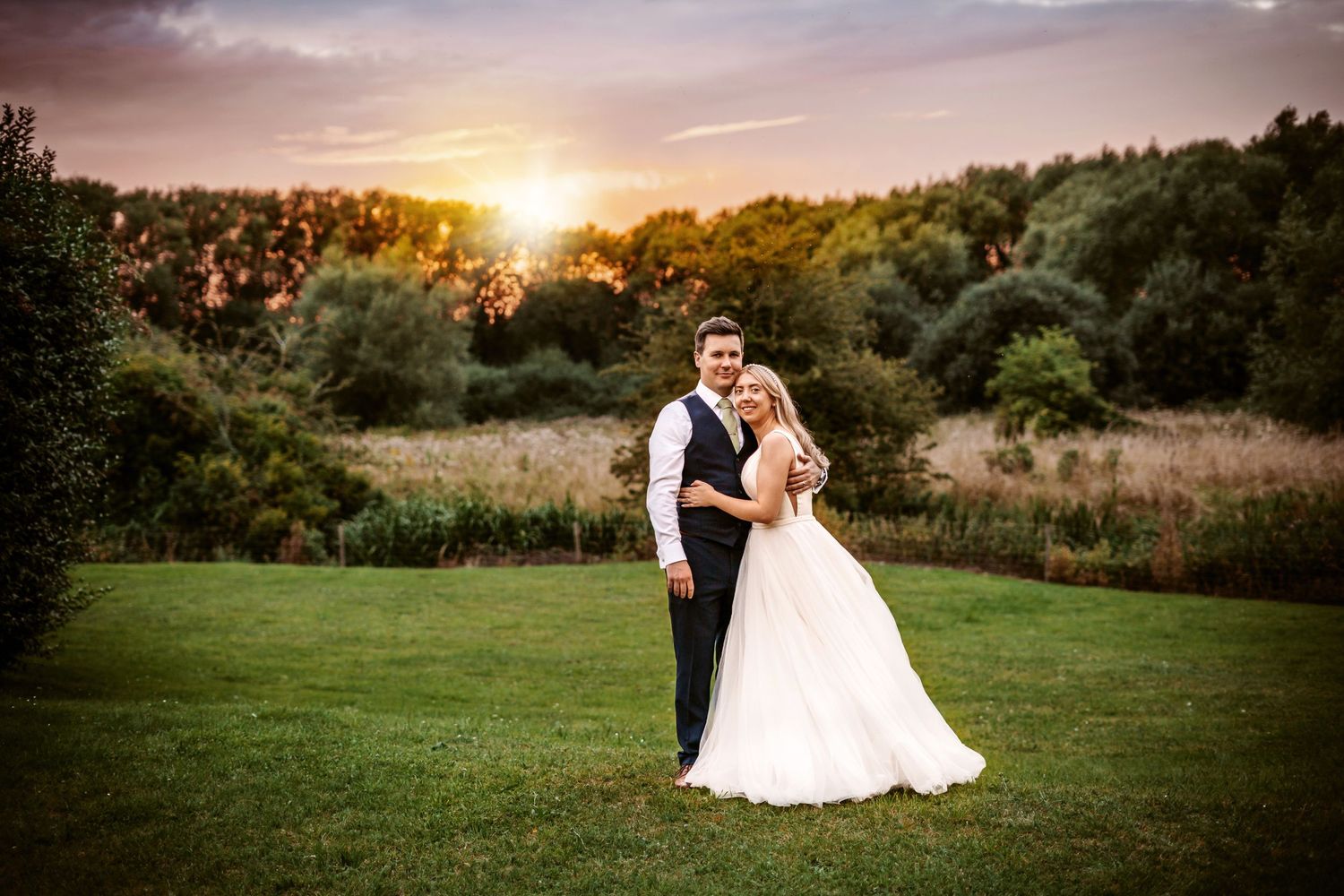 Scenic sunset wedding portrait on a lush green lawn with forest background.