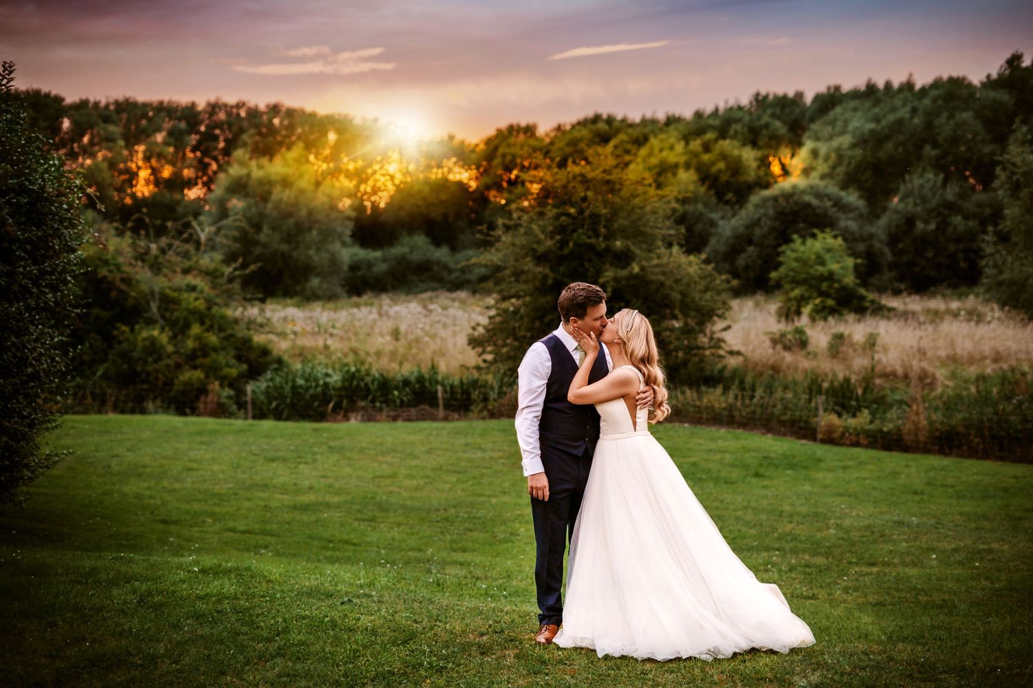 Golden hour wedding portrait in a scenic meadow with trees and dramatic sky.
