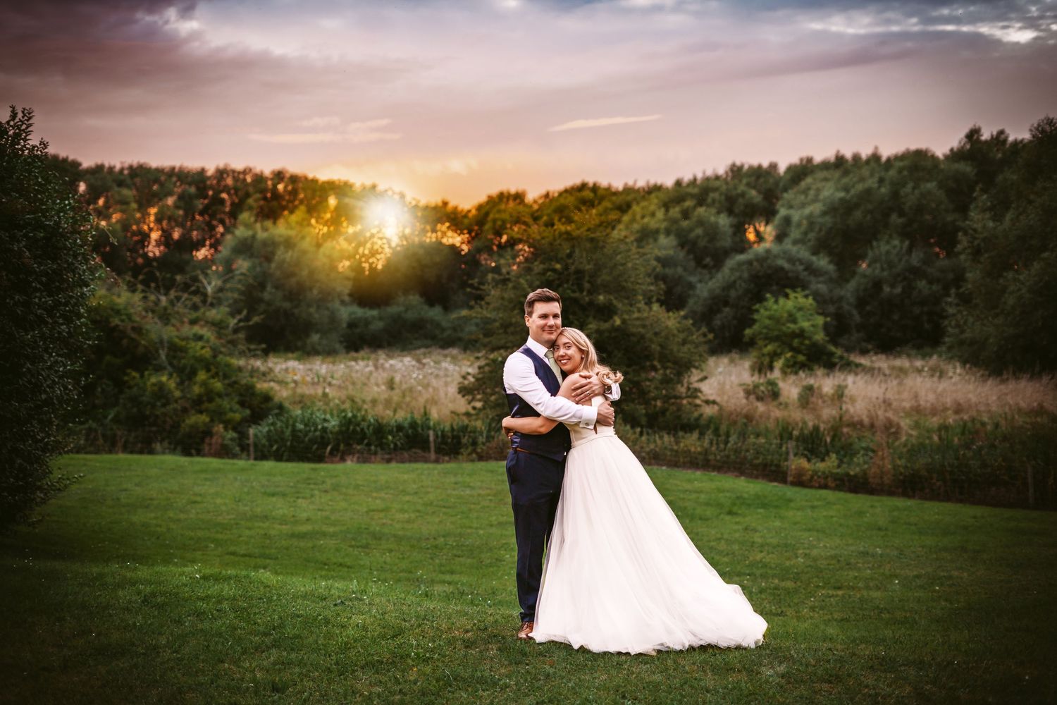 Romantic sunset wedding portrait on rolling green hills with wooded background.