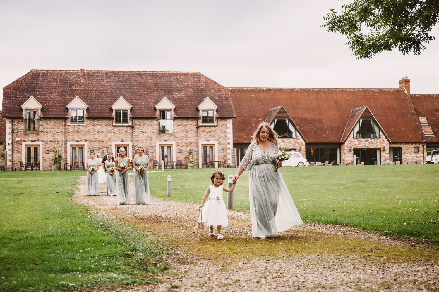 Wedding party walking along gravel path in front of historic stone building with dormers.