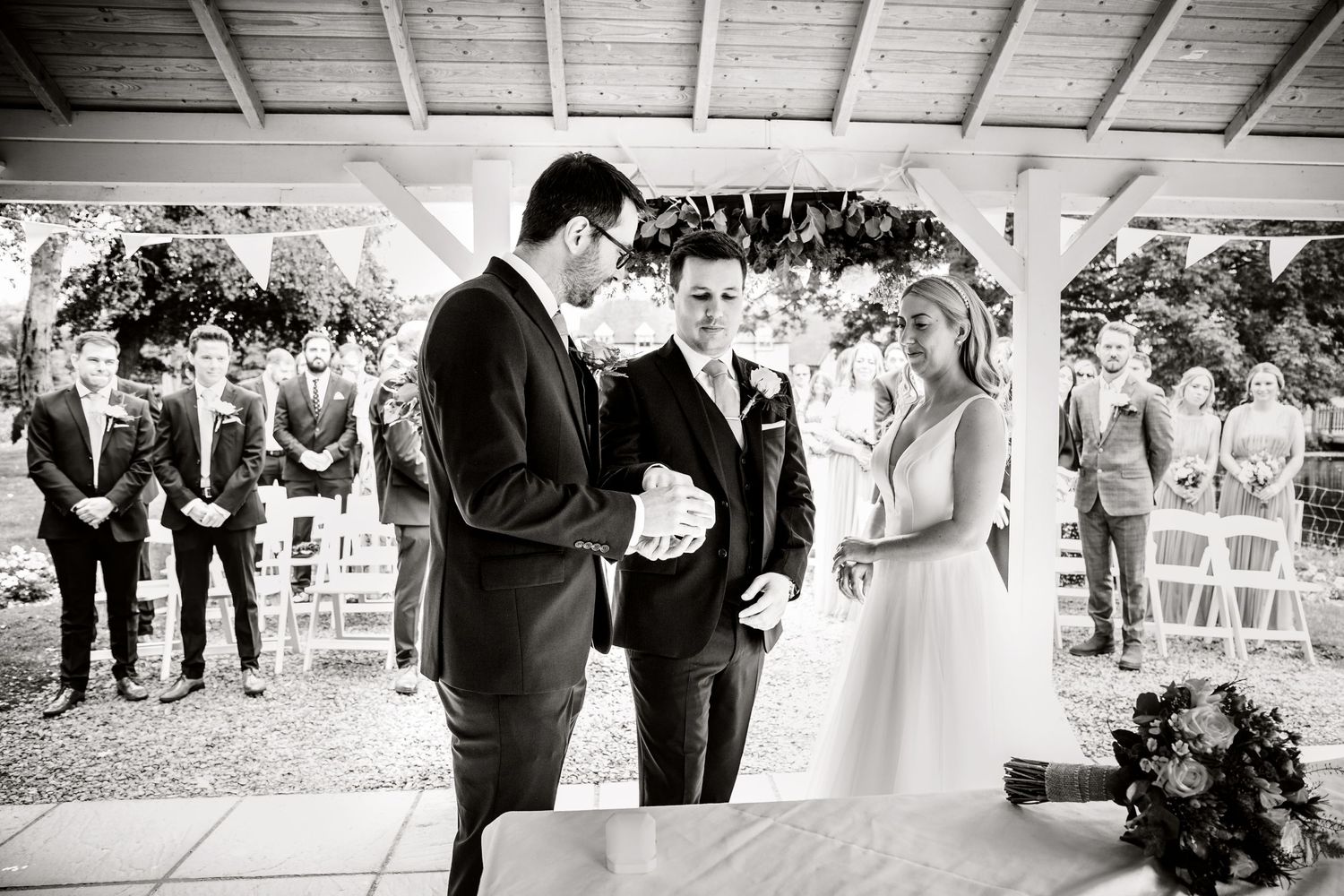 Black and white photo of wedding ceremony under decorated pavilion with florals.