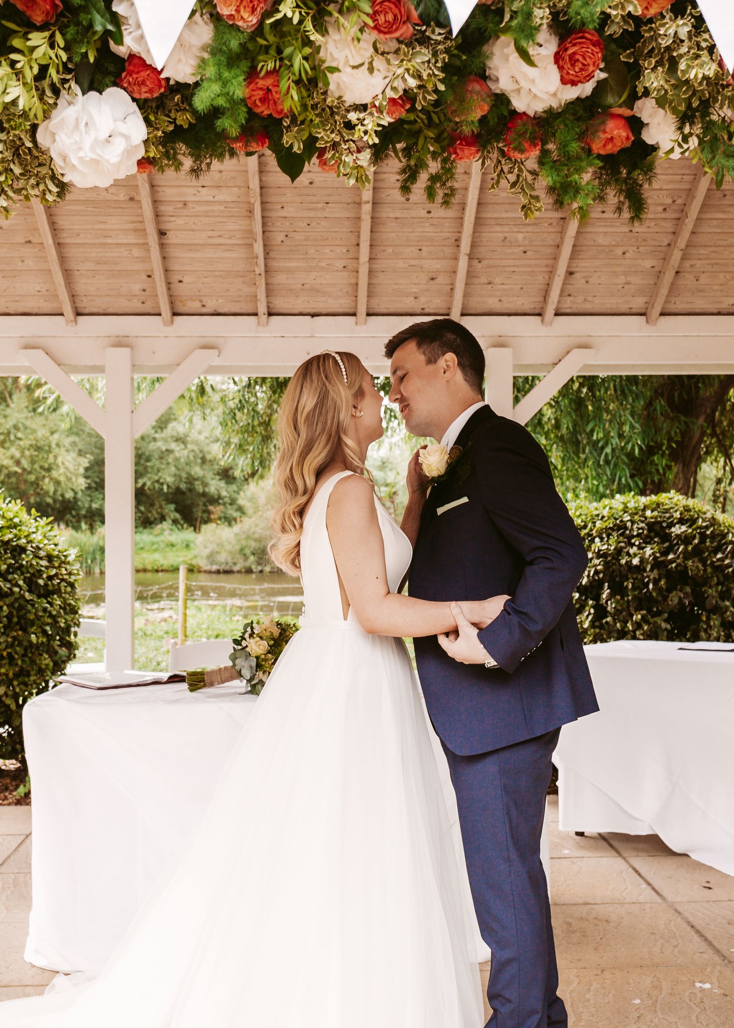 Intimate wedding ceremony under a floral-decorated gazebo with red and white roses and greenery.