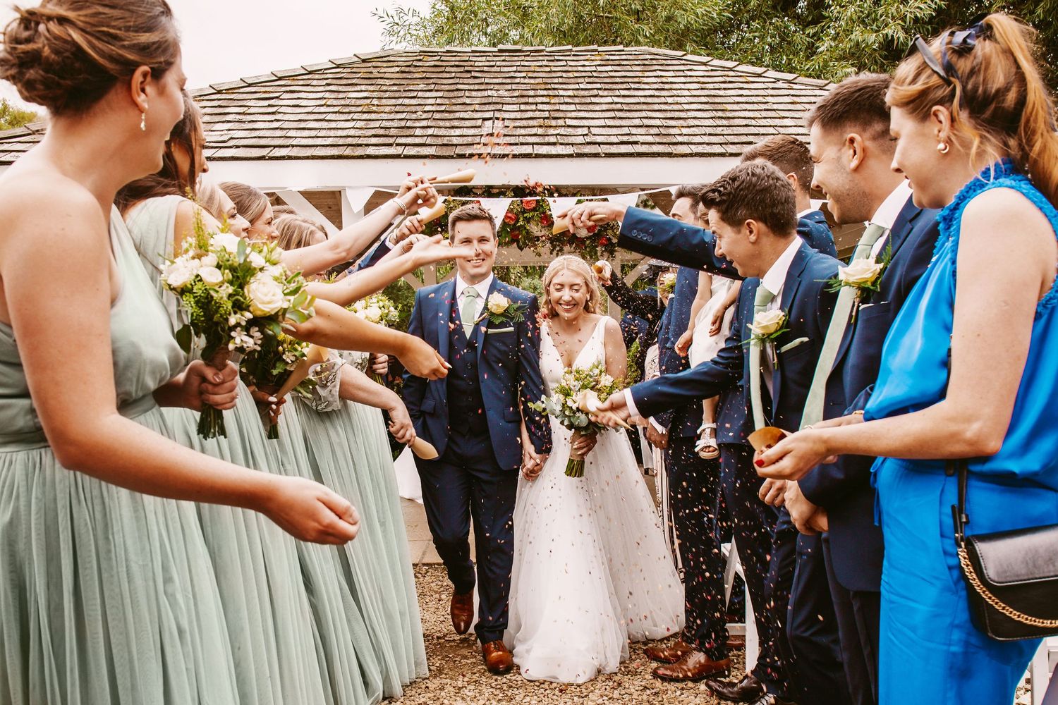 Wedding guests shower newlyweds with confetti along a garden pathway.