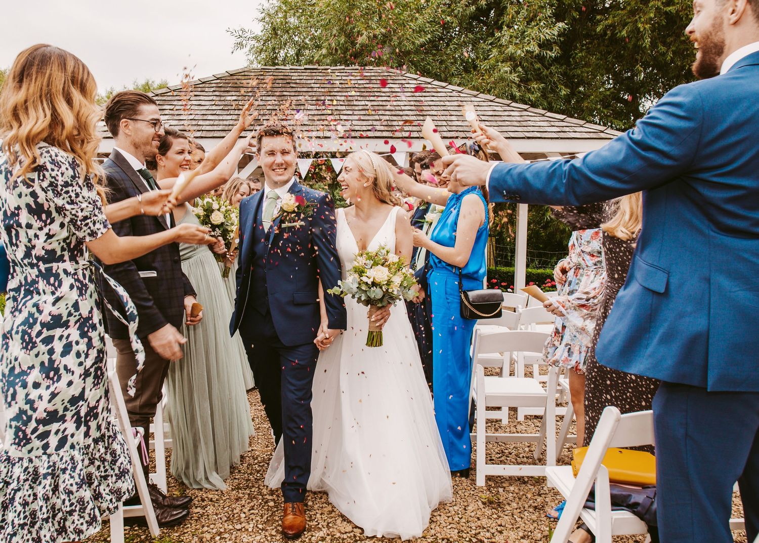 Joyous outdoor wedding celebration with guests throwing confetti at a garden venue.