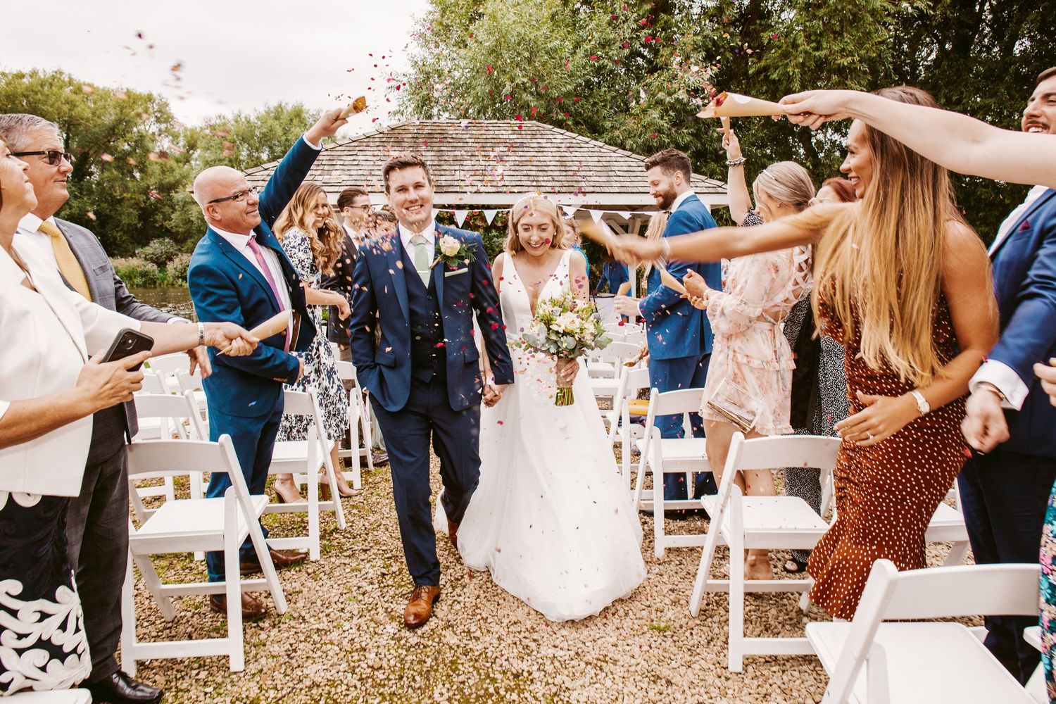 Festive wedding recessional with guests showering couple in confetti on outdoor path.