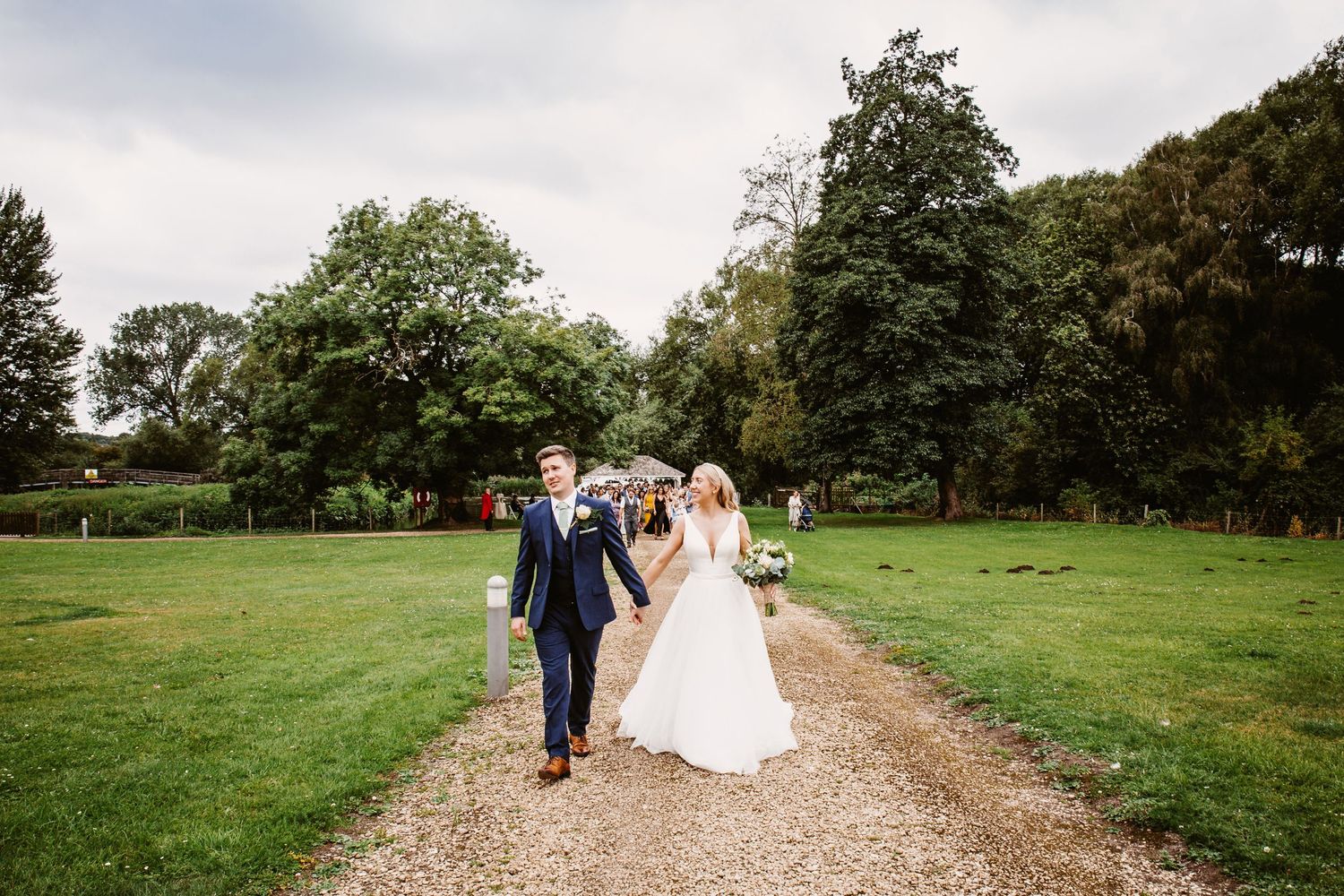 Couple walking along gravel path through lush green garden landscape.