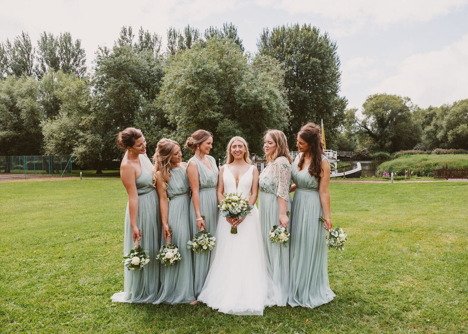 Wedding party stands together on lawn with bridesmaids wearing flowing pale blue dresses.