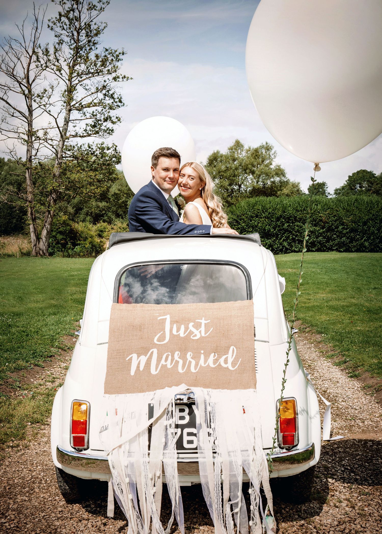 Newlyweds pose in vintage white Fiat decorated with Just Married sign and streamers.
