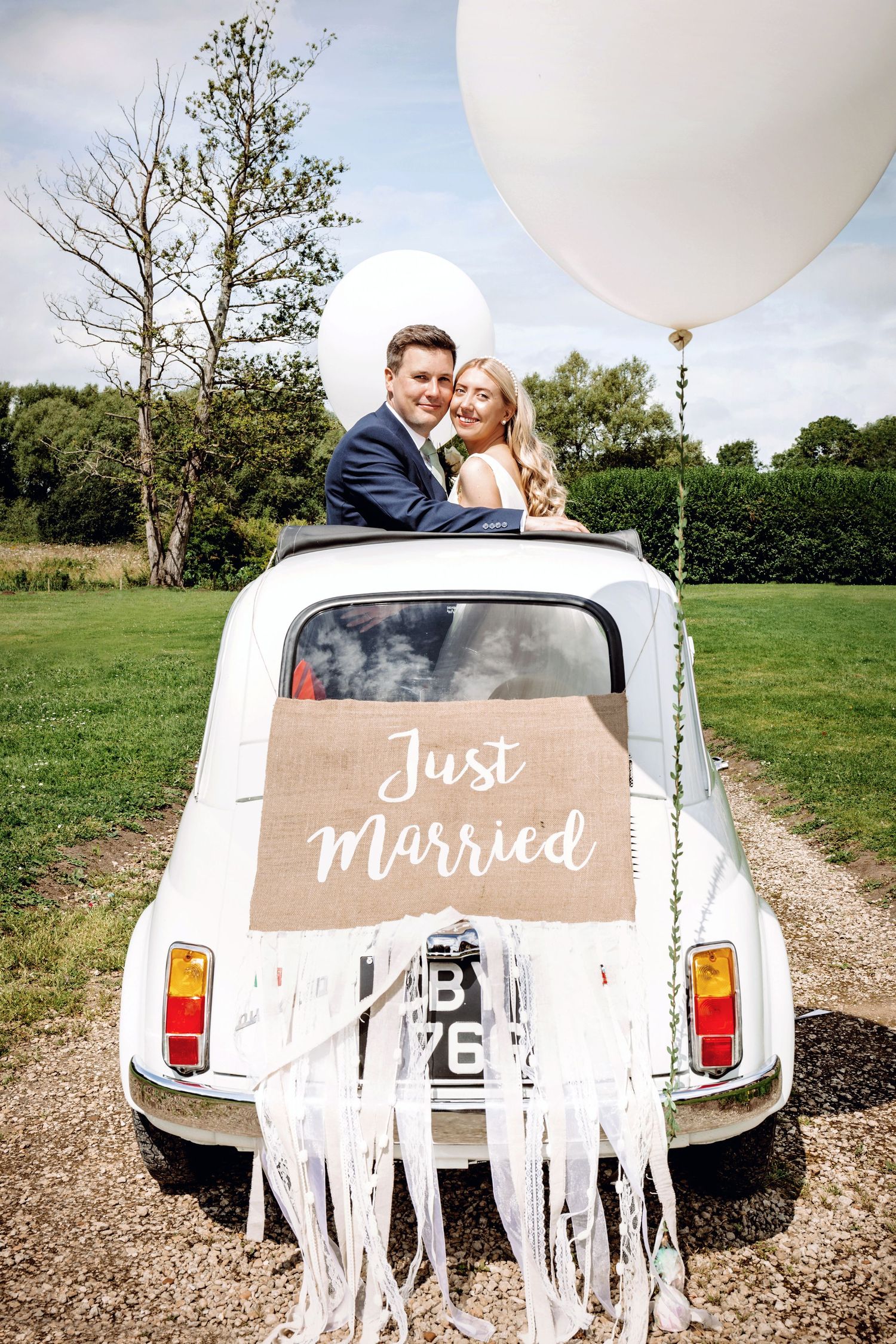 Couple poses in decorated vintage Fiat 500 with Just Married sign and white streamers.