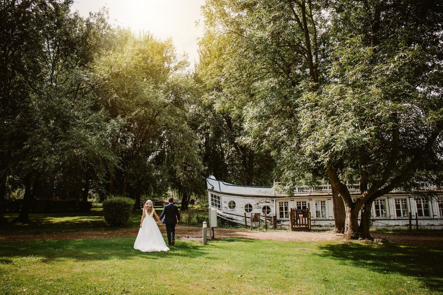 Wedding ceremony setup in lush garden with white decorations and natural sunlight.