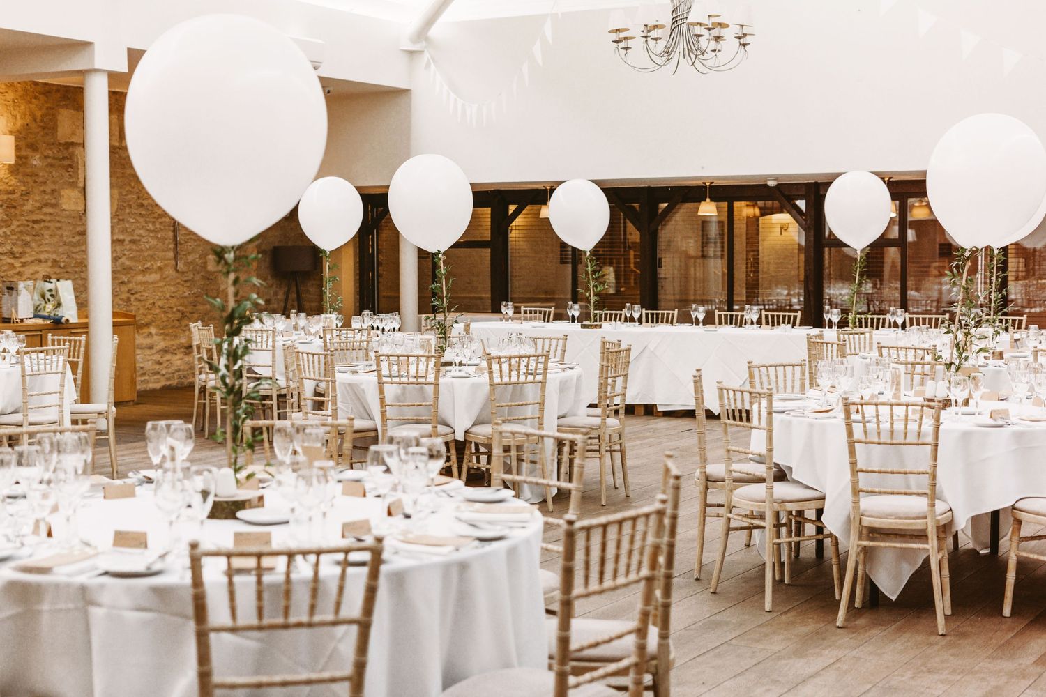 Elegant wedding reception hall with white balloons, chandeliers and chiavari chairs.