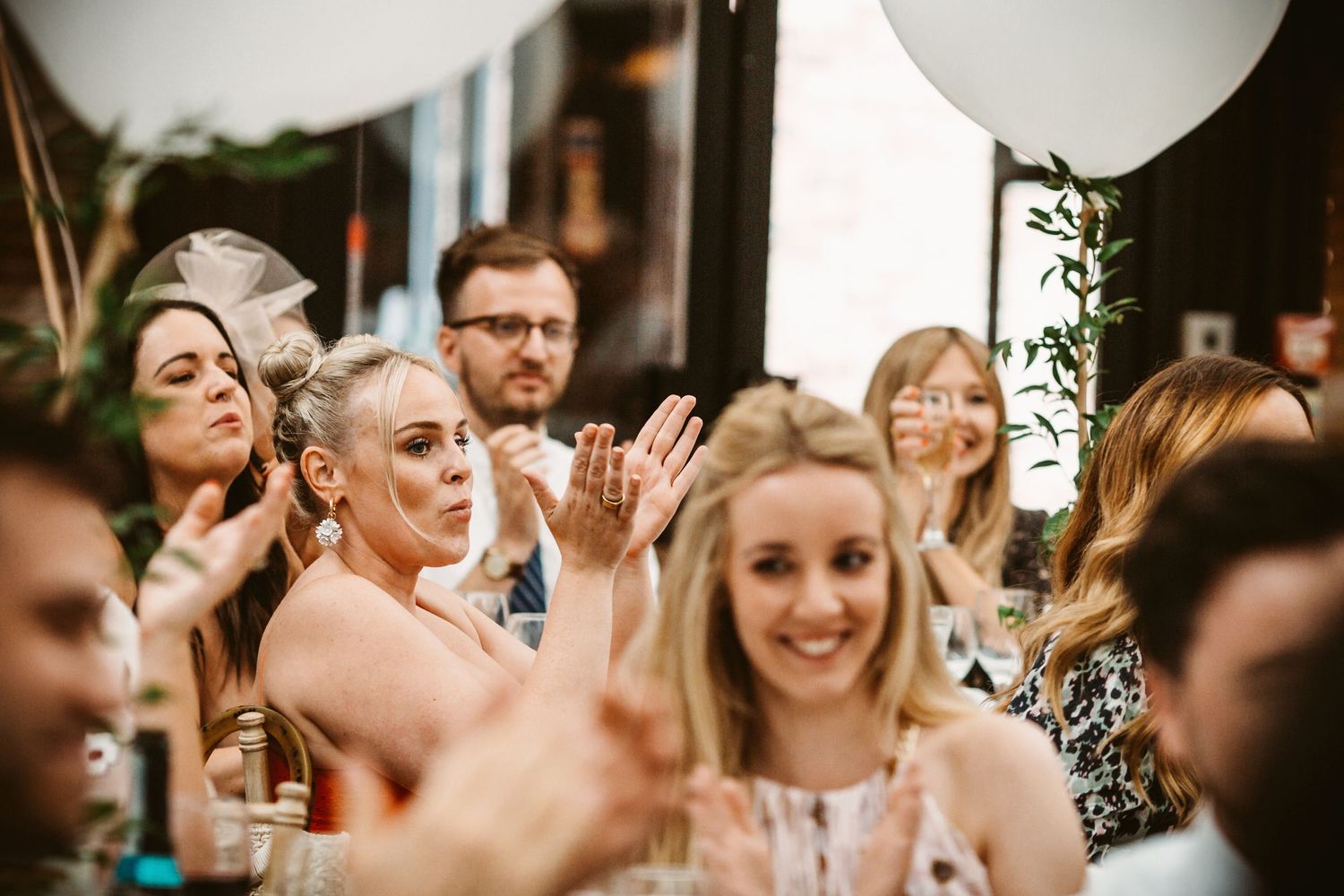 Wedding guests laugh and celebrate with champagne glasses and white balloons at an elegant reception.