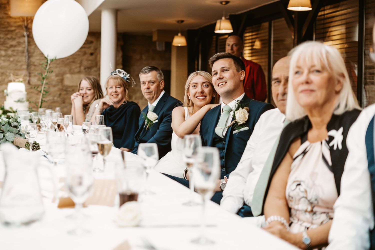 Reception guests seated at long tables decorated with white balloons enjoy the wedding celebration.