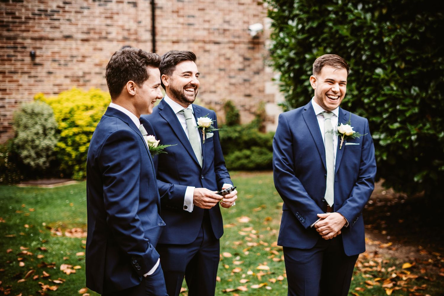 Groomsmen sharing a laugh together during outdoor wedding celebration.