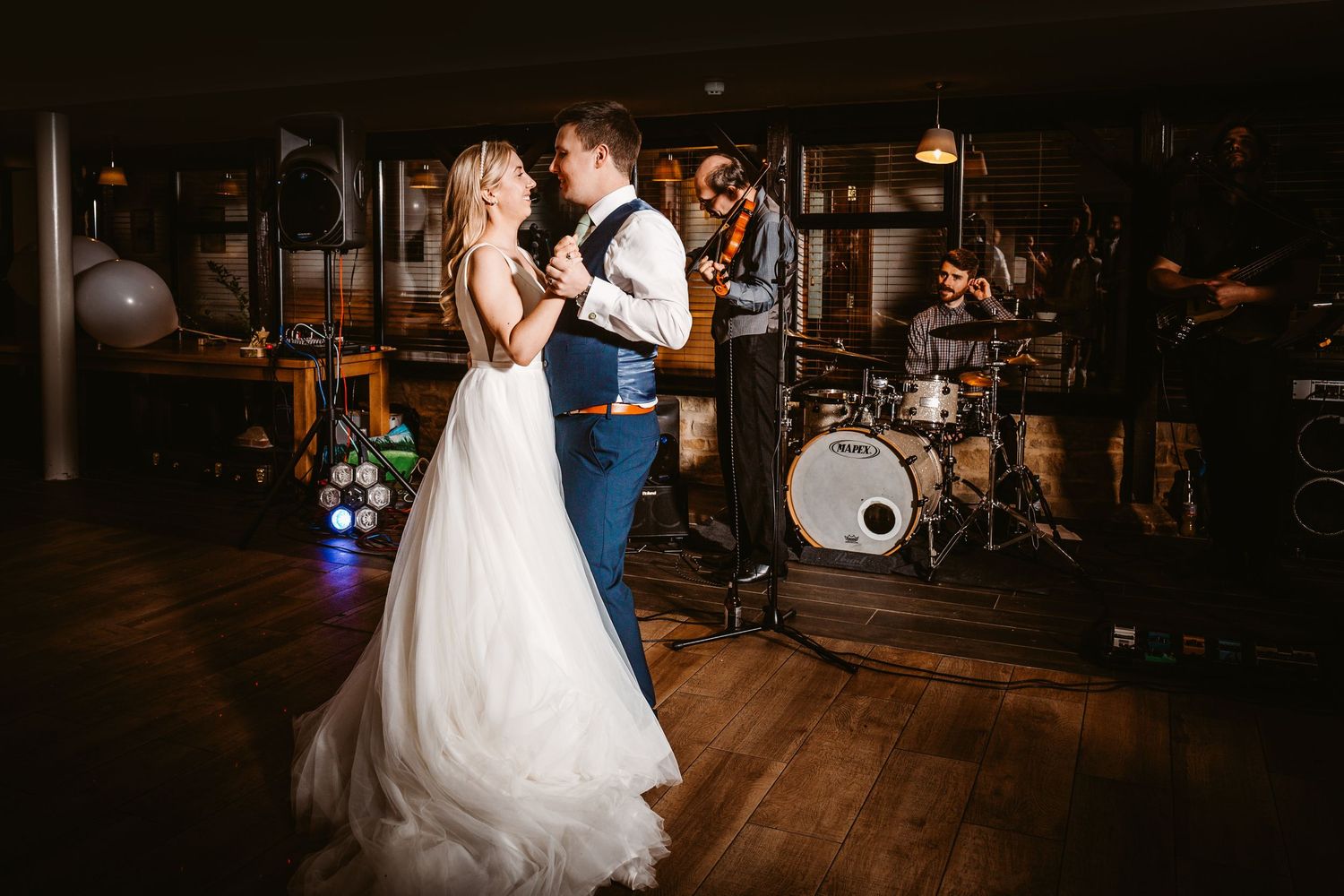 Romantic first dance moment in dimly lit reception venue with drum kit visible in background.
