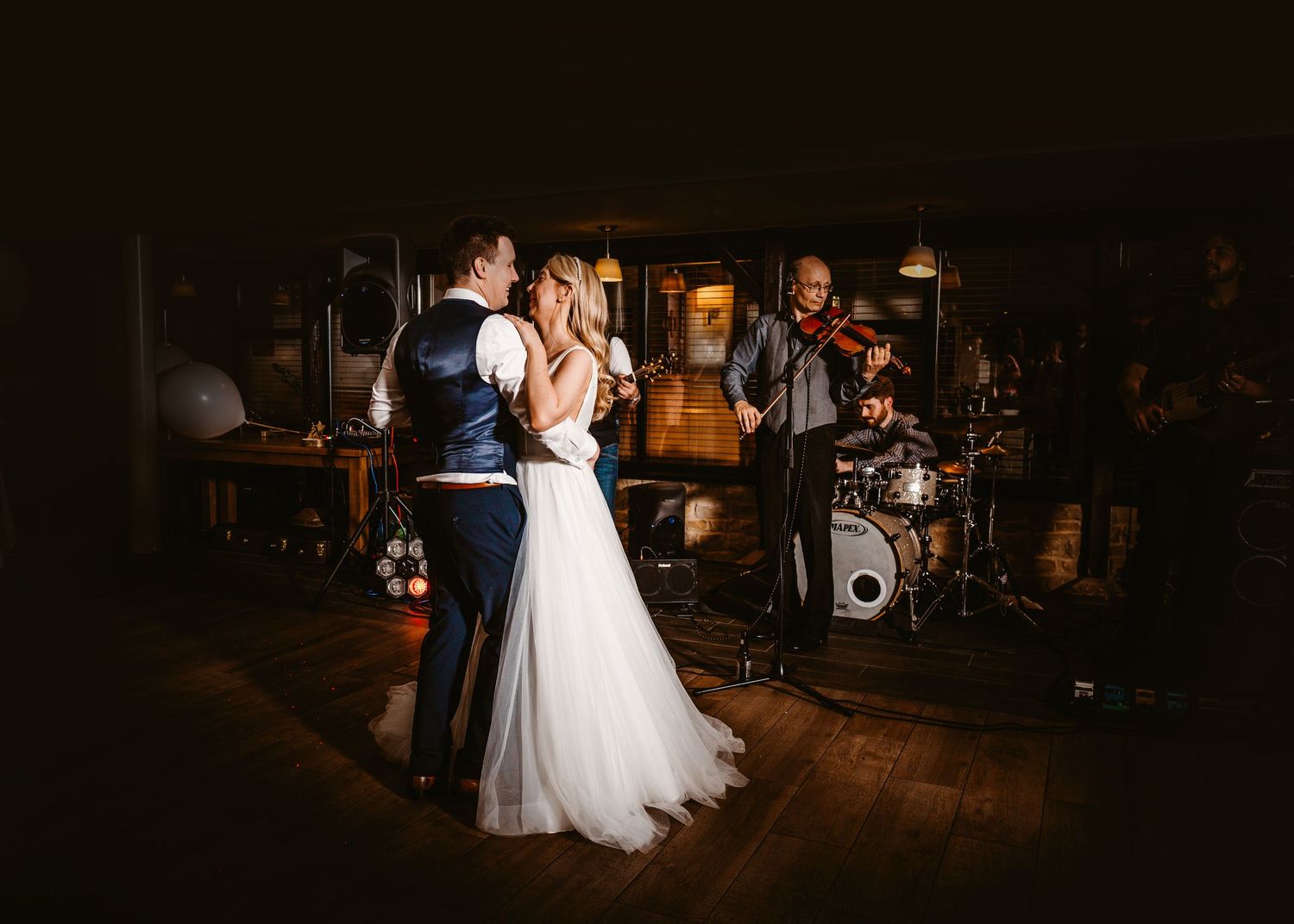 Wedding celebration on wooden dance floor with live band performing in background.