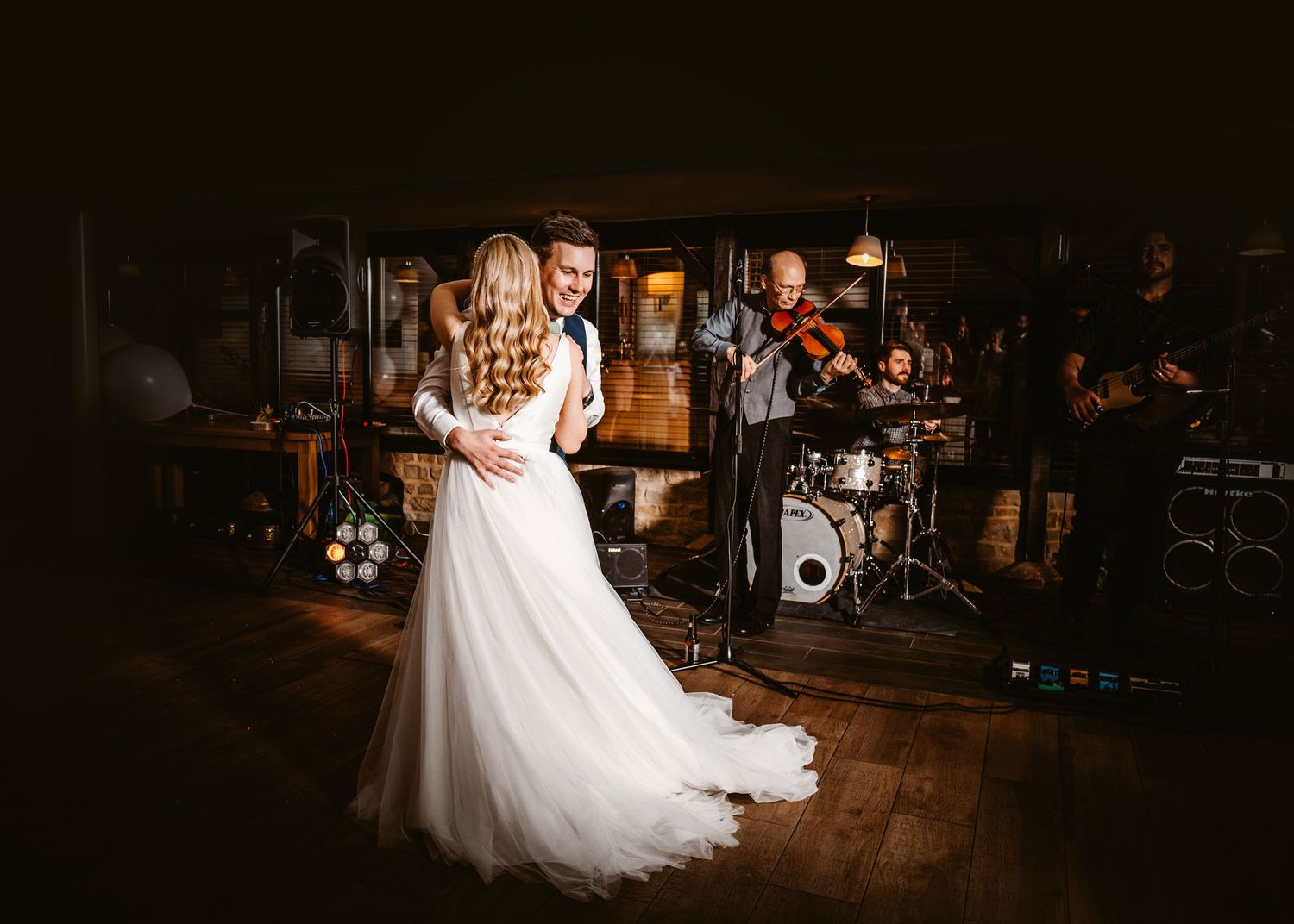 Live band performs at wedding reception as couple dances on wooden floor.
