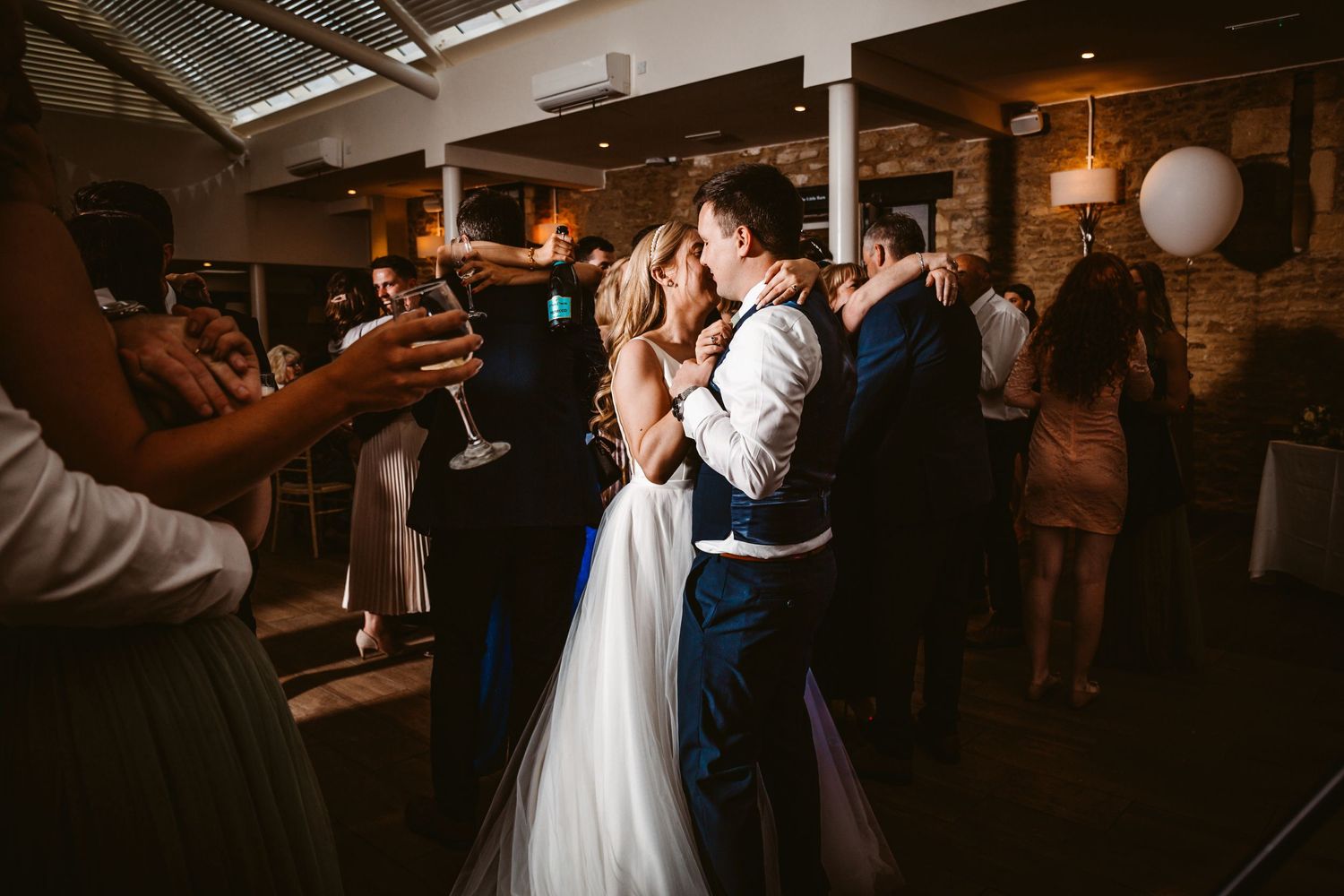 A tender dance scene at a wedding reception with guests watching in a rustic brick-walled venue.