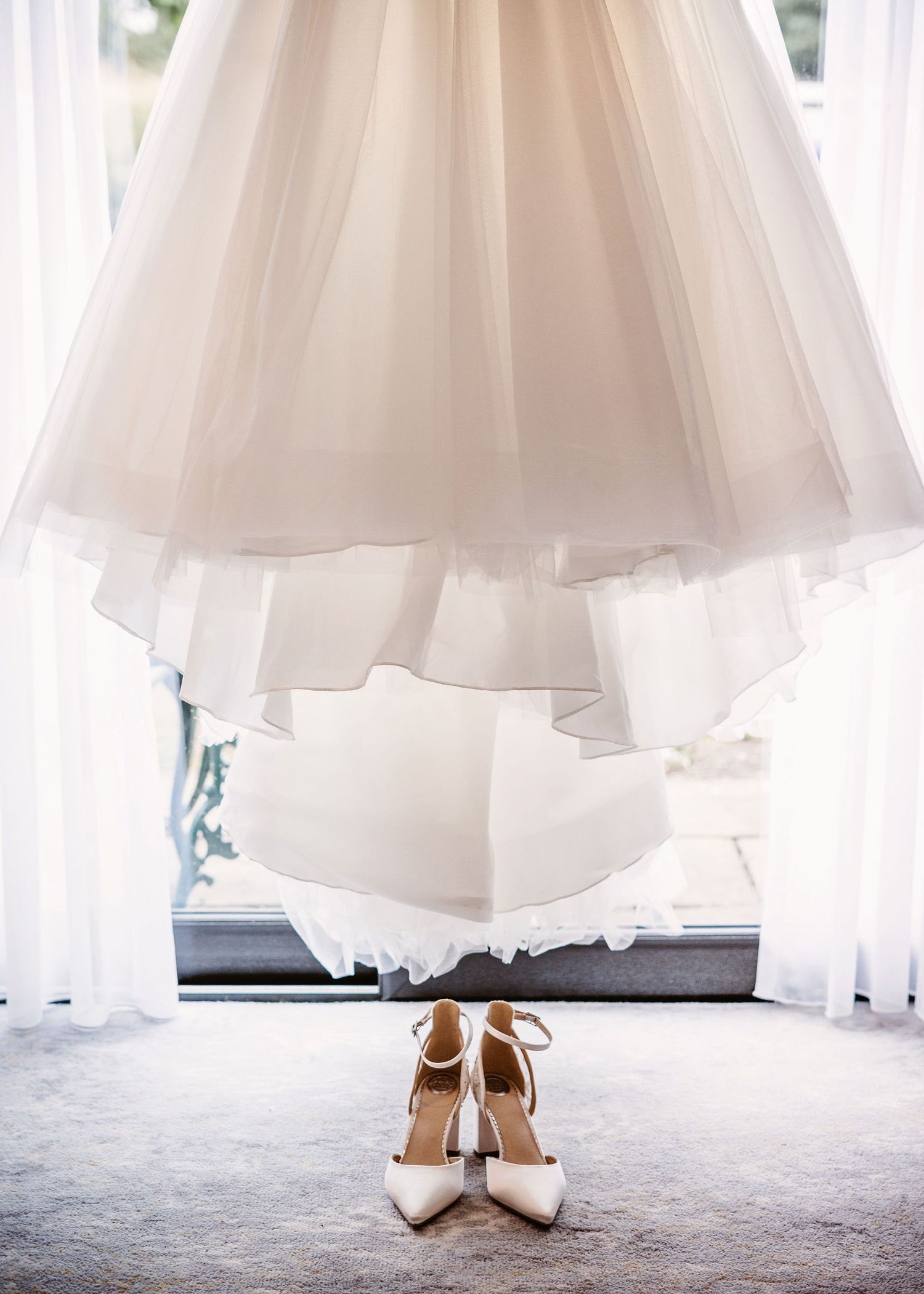 White wedding dress and heels artistically photographed against window light.