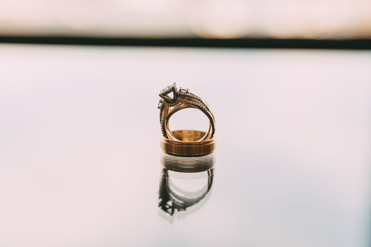 Gold diamond engagement ring and wedding band reflected on glossy surface in close-up shot.